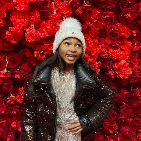 a woman standing in front of red flowers wearing a black jacket and ...