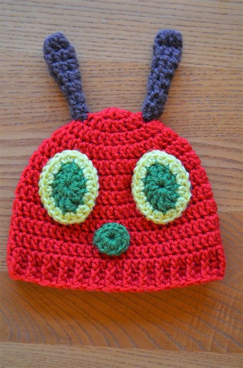 a crocheted red hat with two green eyes on top of a wooden table