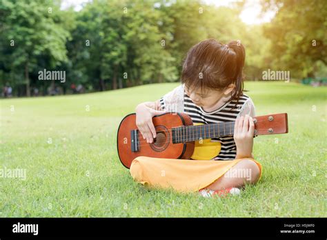 Asian little kids girl sitting on grass and play ukulele in park. Kids ...