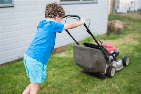 Image of Boy pushing lawn mower mowing lawn - Austockphoto