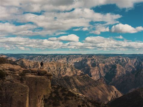 a man standing on the edge of a cliff looking out at mountains and ...