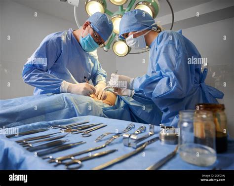 Doctor and assistant performing aesthetic surgery in operating room with various stainless steel ...