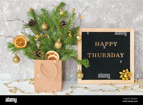 Happy Thursday text on black letter board and festive bouquet of fir branches with christmas ...