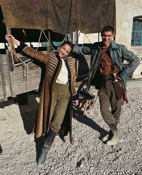 two men standing next to each other in front of an old wooden structure with ropes hanging from it