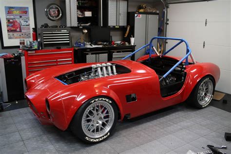 a red sports car in a garage with tools on the floor and cabinets behind it