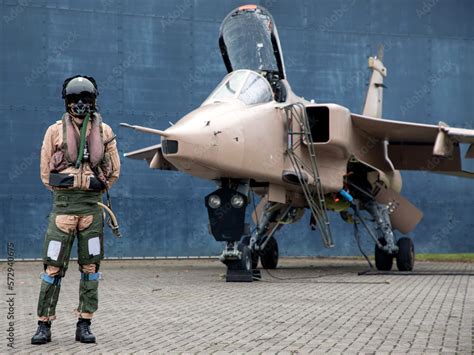 Fighter pilot standing with Military fighter Jet wearing flying helmet, suit and dark visor with ...