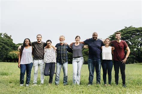 a group of people standing in the grass posing for a photo with their arms around each other