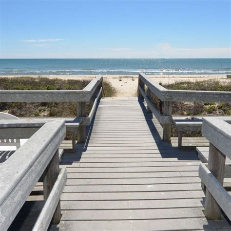 a wooden walkway leading to the beach with benches on each side and sand dunes in the background