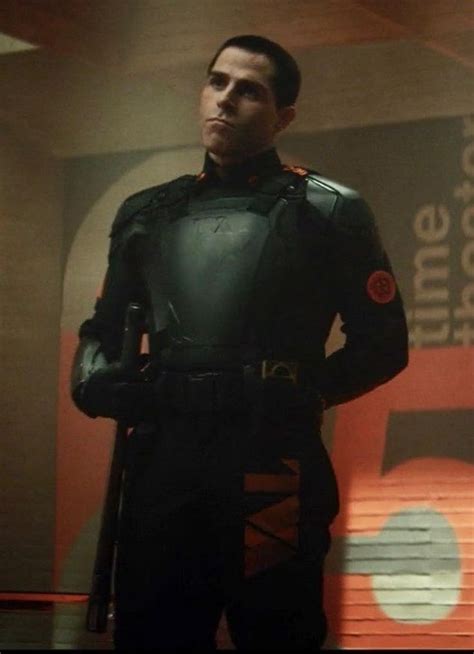 a man standing in front of a sign wearing a black suit and red helmet with his hands on his hips