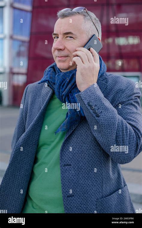 Portrait of pleased middle-aged man standing near modern building with red glass facade in city ...