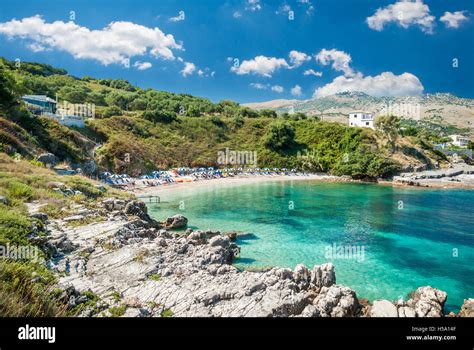 Kassiopi Beach, Corfu Island, Greece. Sunbeds and parasols (sun umbrella) on the beach. Tourists ...