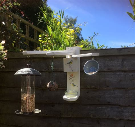 a bird feeder hanging from the side of a wooden fence next to a bird feeder