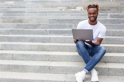 Young smiling successful african american male student with lucky face working on laptop ...