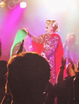 a woman in a costume standing on stage with her arms out to the side while people watch