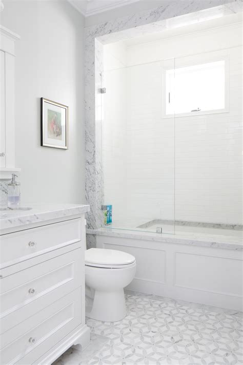 This white bathroom features a unique white and gray tile pattern, a stone slab counter top, and ...