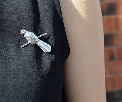 a woman wearing a black dress with a silver bird brooch on it