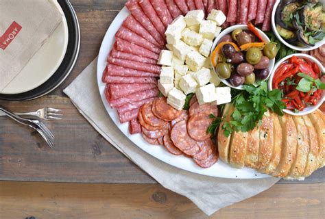 an assortment of meats and cheeses on a platter next to a plate with bread