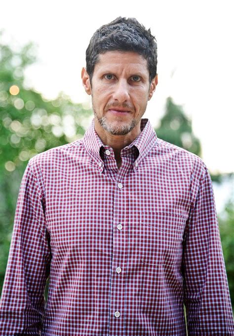 a man wearing a red and white checkered shirt standing in front of some ...