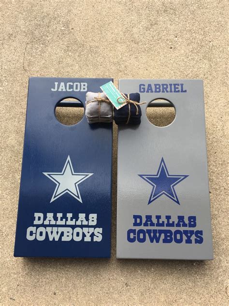 two blue and gray cornhole game boards with cowboys logos on them sitting on the ground