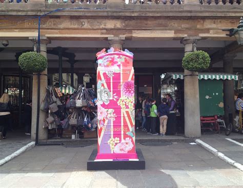 a tall pink and purple object sitting in front of a building with people standing around it