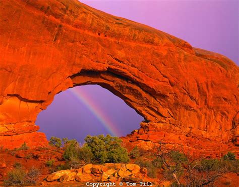 a rainbow shines in the sky over a rock formation with an arch like ...