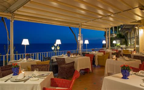 an outdoor dining area with tables and chairs overlooking the ocean at night, lit by lamps