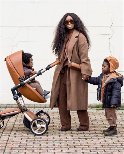 a woman holding hands with a baby in a stroller and another child standing next to her