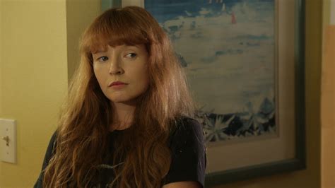 a woman with long red hair standing in front of a painting and looking at the camera