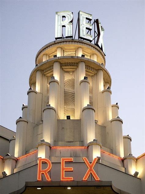 the top of a tall building with a neon sign on it's side that reads, rex french art deco