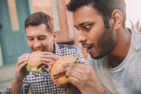 Emotional Young Men Eating Gourmet Hamburgers Outdoors Stock Image - Image of food, bottle: 91335523