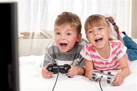 Young boy and girl lying on a bed enjoying playing video games together - Your Health