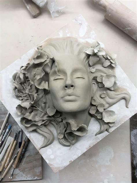 a clay sculpture of a woman's face with flowers in her hair