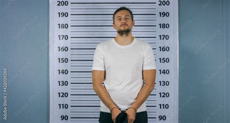 Arrested a man in handcuffs standing near a white board with a scale. Mugshot Stock Photo ...