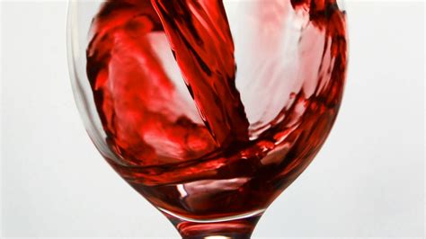 Wine. Red wine pouring in wine glass over dark background. Rose wine pouring from the bottle ...