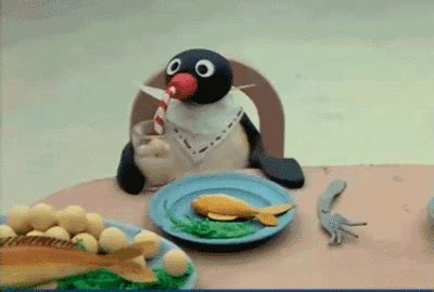 a penguin sitting at a table with plates and food in front of him, eating