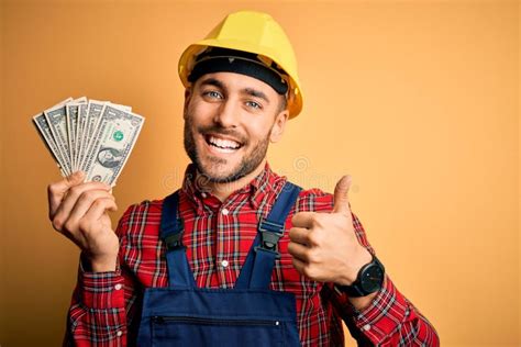 Young Builder Man Wearing Safety Helmet Holding Dollars As Payment Over Yellow Background Happy ...
