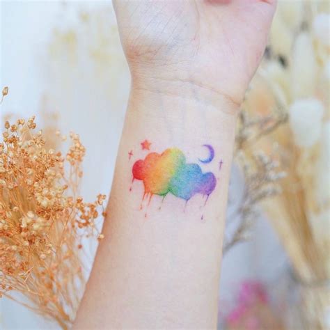 Watercolor rainbow cloud tattoo on the wrist.