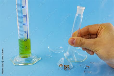 Laboratory experiment. Hand holding broken lab flask glass and measurement glass smoking on blue ...