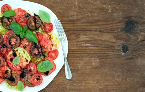 Ripe village heirloom tomato salad with olive oil and basil over rustic wooden background, top ...