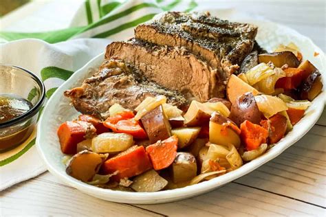 a white plate topped with meat and veggies next to a bowl of sauce