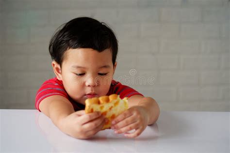 Cute Little Asian Boy Has an Bored Expression and is Eating Bread on a White Dining Table Stock ...