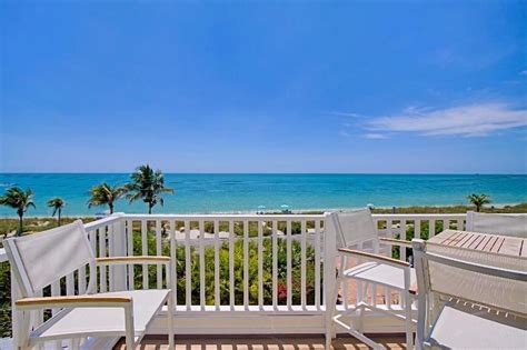 two white chairs sitting on top of a wooden deck next to the ocean and ...