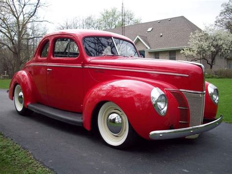 an old red car parked on the side of a road in front of a house