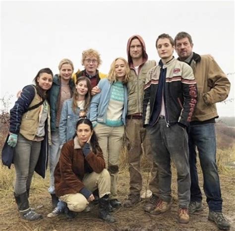 a group of people standing next to each other on top of a dirt field with trees in the background