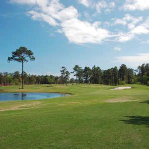 a golf course with water and trees in the background on a sunny day, surrounded by blue skies