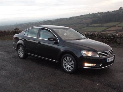 a black car parked on the side of a road next to a stone wall and field