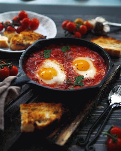 two eggs are in a skillet with tomato sauce and bread on the table next to it