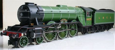 a green and black model train on display in a room with white flooring,