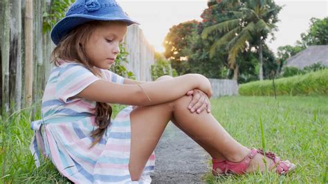 Happy little girl sitting on the grass and playing in summer garden ...