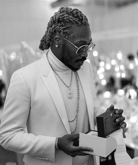 a man in a white suit holding a box and looking down at his cell phone